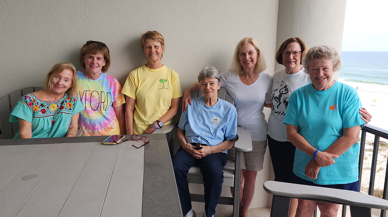 A group of women gather on a balcony overlooking the ocean.