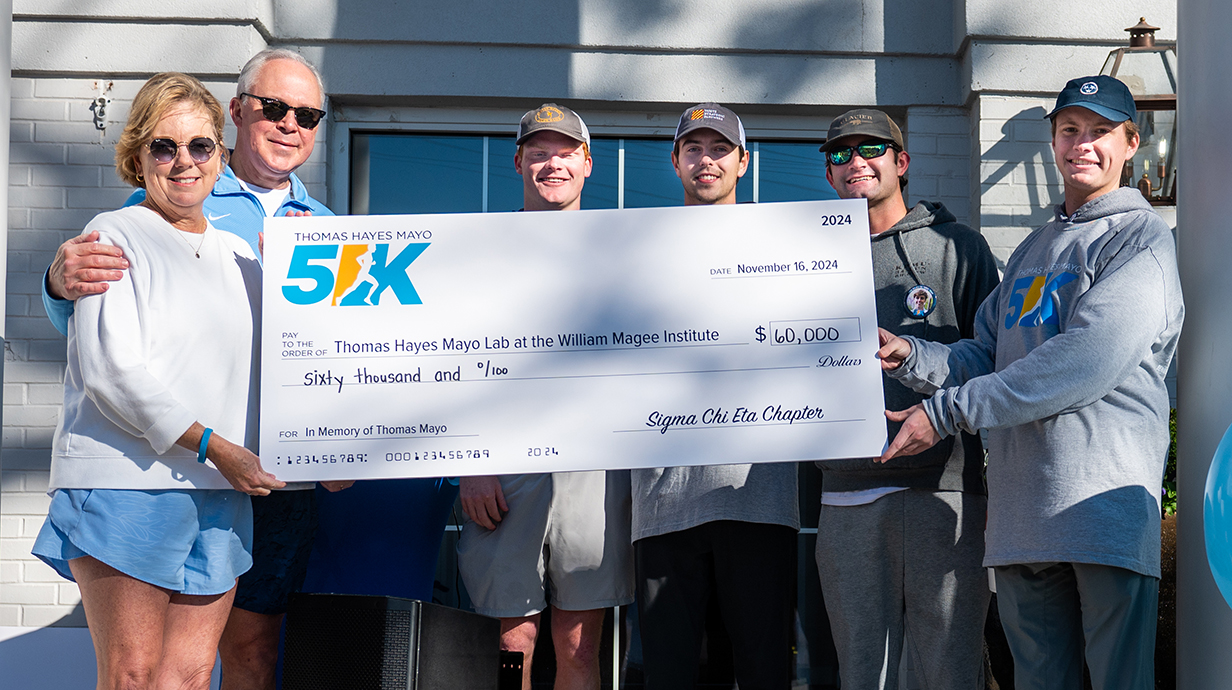 Five men and a woman hold a giant check from a fundraiser.