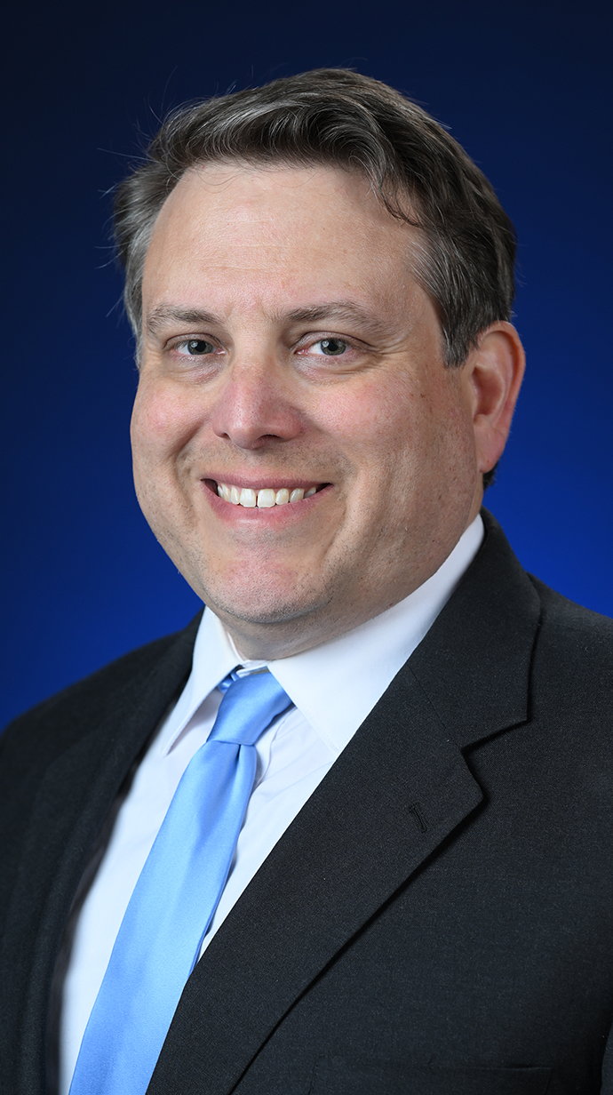 Headshot of a man wearing a dark blue suit with a light blue tie.