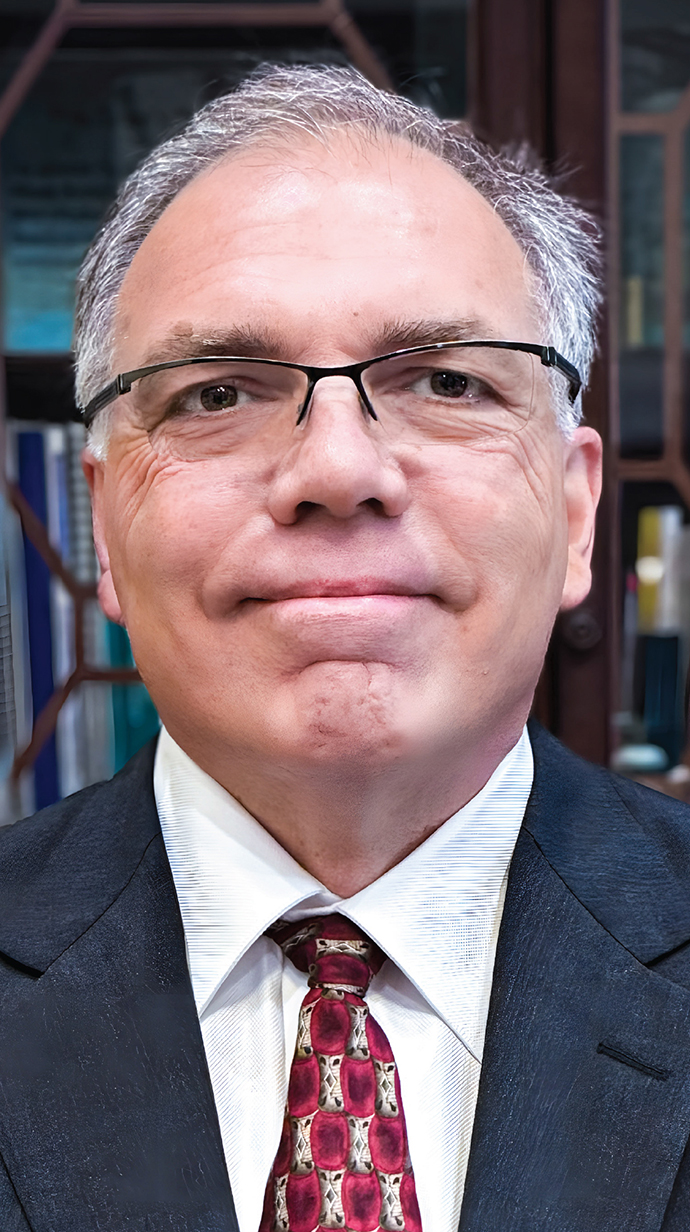 Headshot of a man wearing glasses and a dark blue suit.