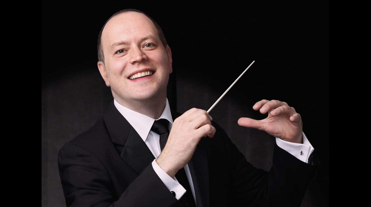 A man wearing a suit holds a conductor's baton.