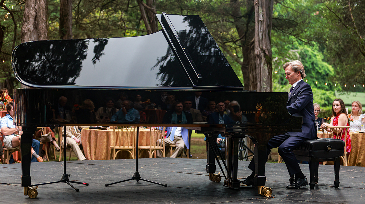 A man plays a piano on an outdoor stage as a crowd watches.