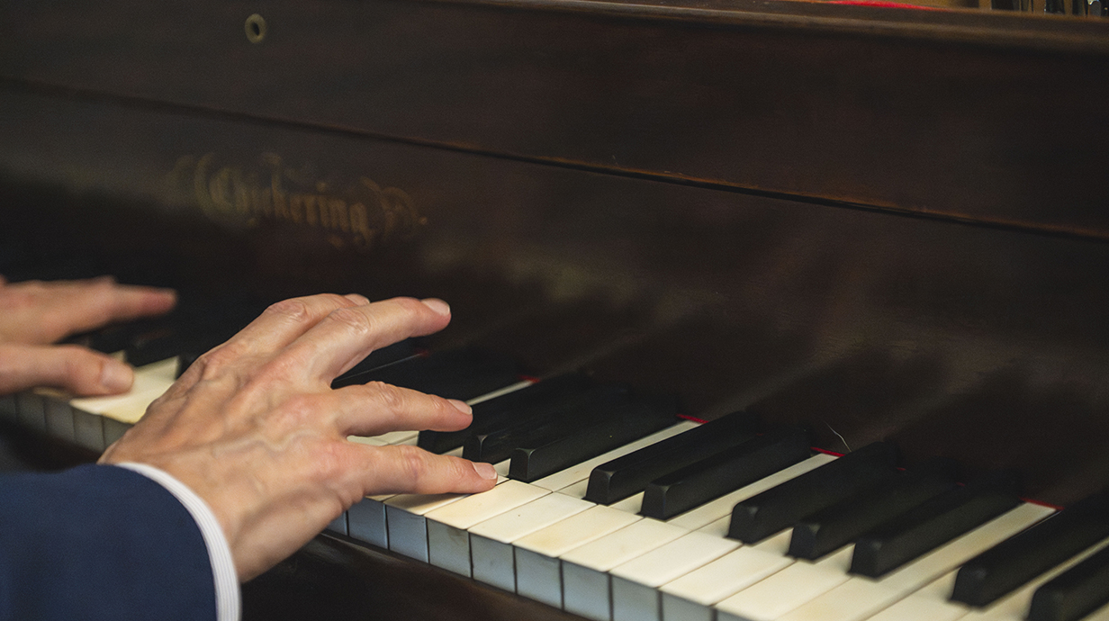 A man's hands rests on a piano keyboard.