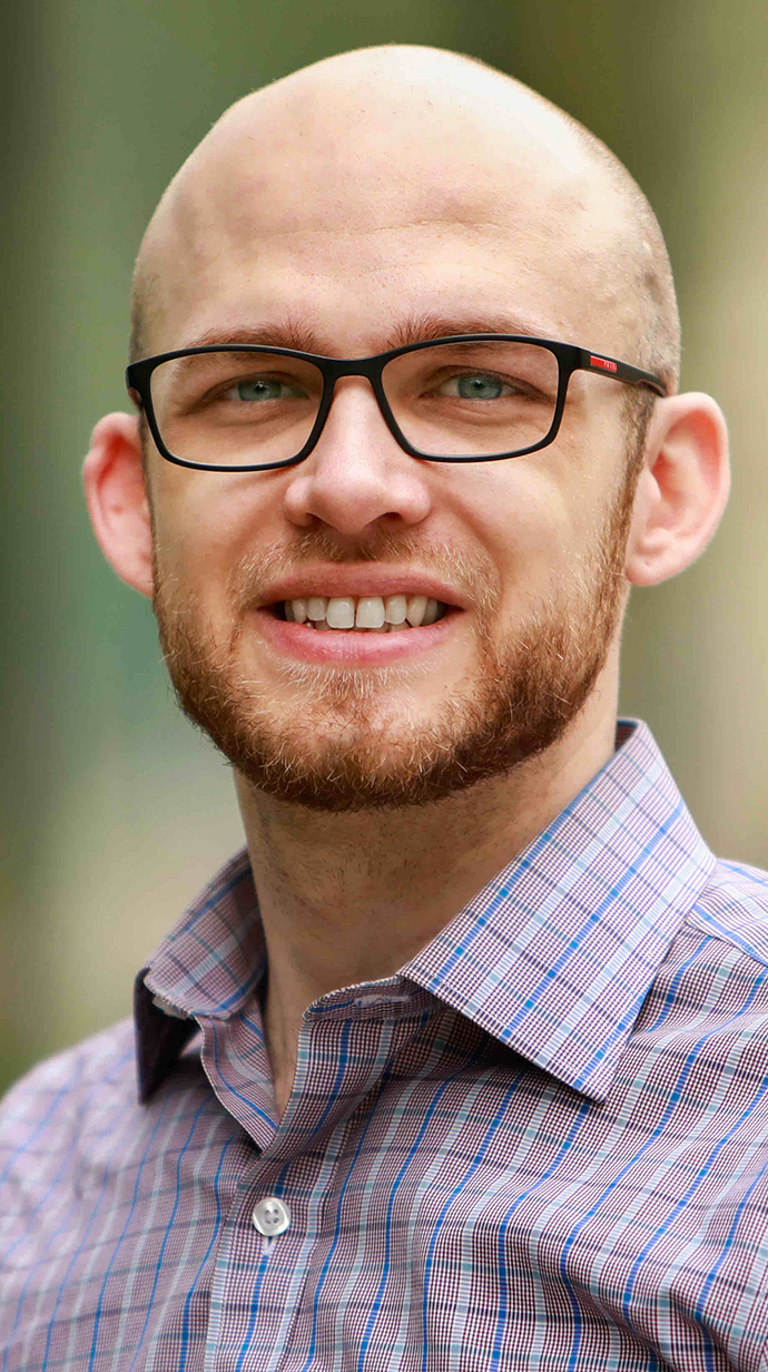 Head shot of a bald man wearing glasses and a patterned shirt.
