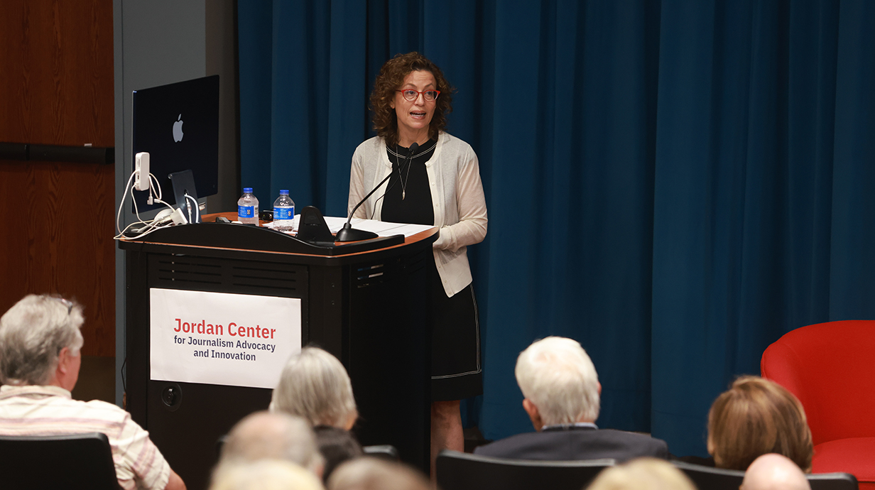 A woman speaks on a stage in an auditorium full of people.