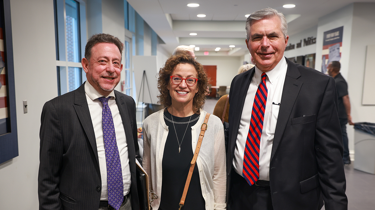 Two men and a woman stand in a hallway.