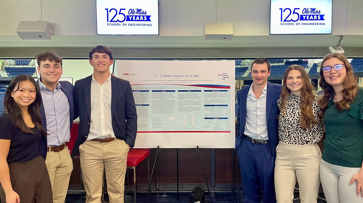 Six young people in business attire stand in front of a presentation poster.