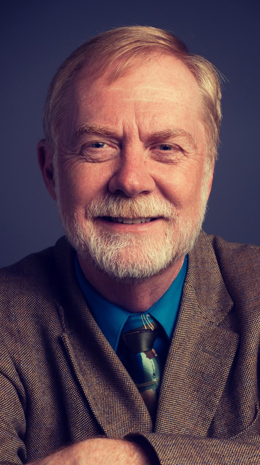 Headshot of a man wearing a brown suit with a blue shirt.