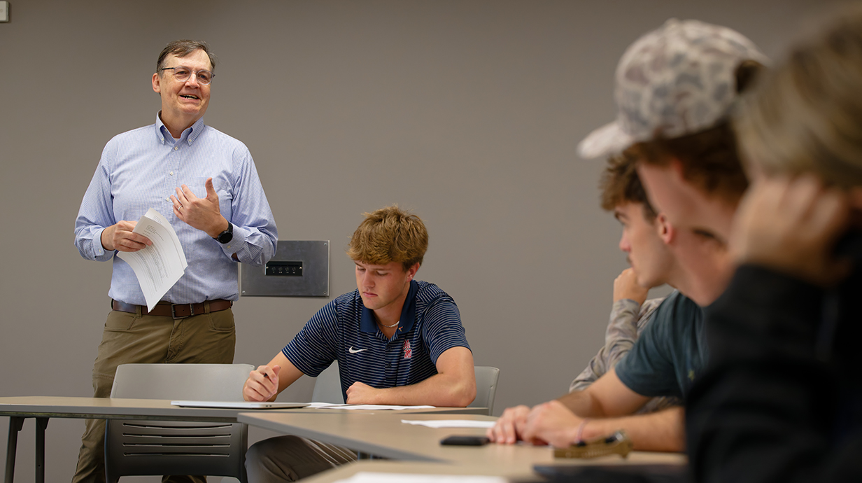 A man lectures in a classroom full of students.