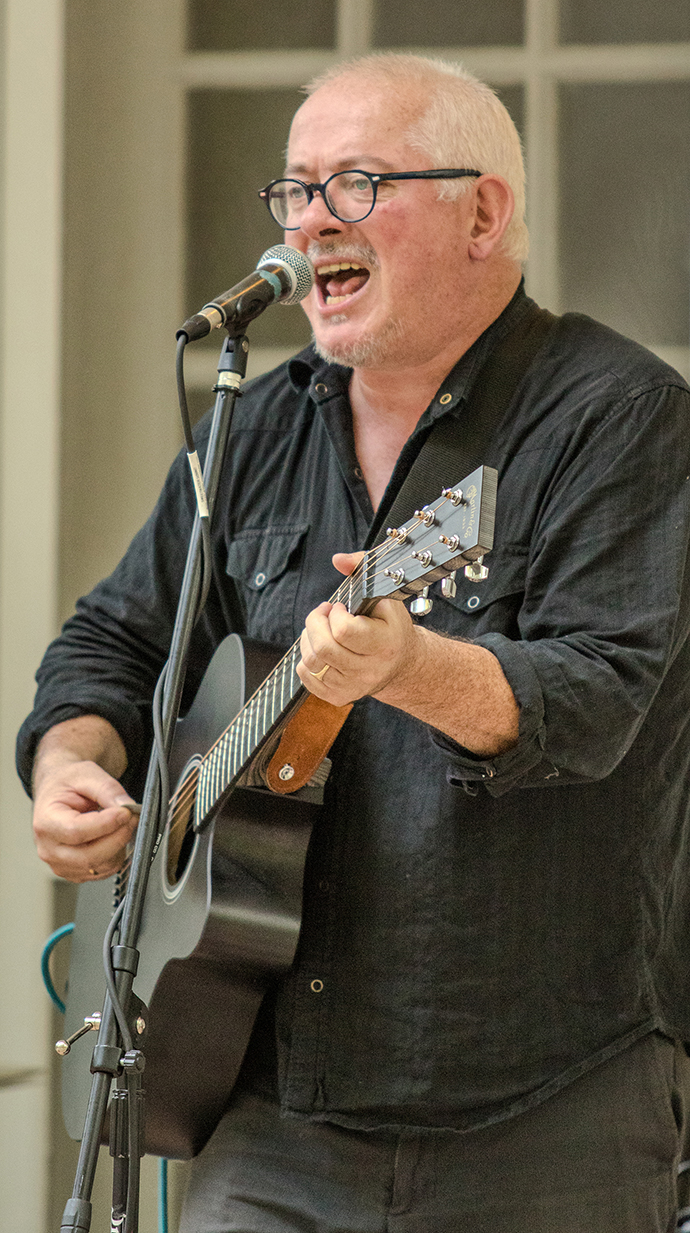 A man plays guitar and sings into a microphone on an outdoor stage.