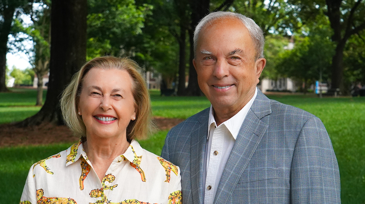 A woman and a man stand in a park dotted with trees.