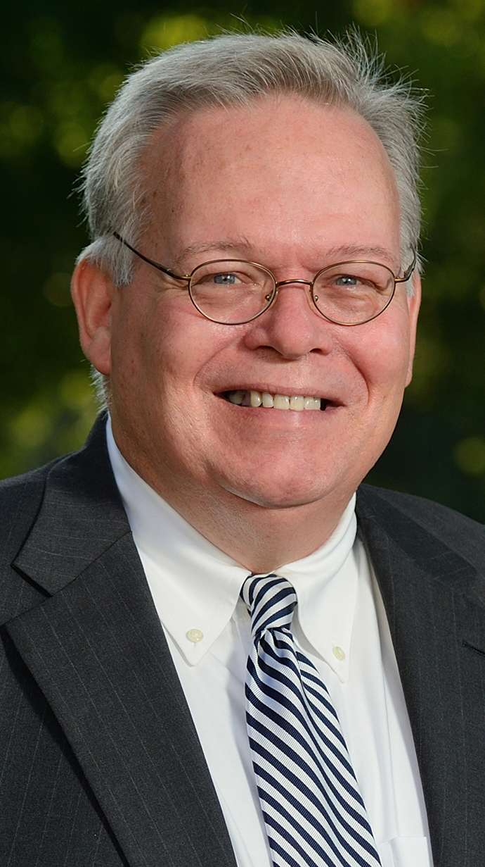 Headshot of a man wearing glasses and a dark suit standing outdoors.