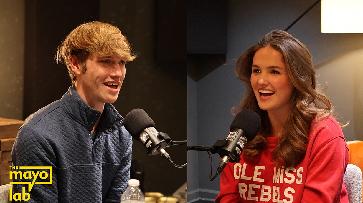 A young man and young woman speak into microphones in a recording booth.
