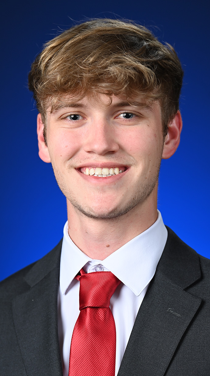 Headshot of a young man wearing a dark suit with a red tie.