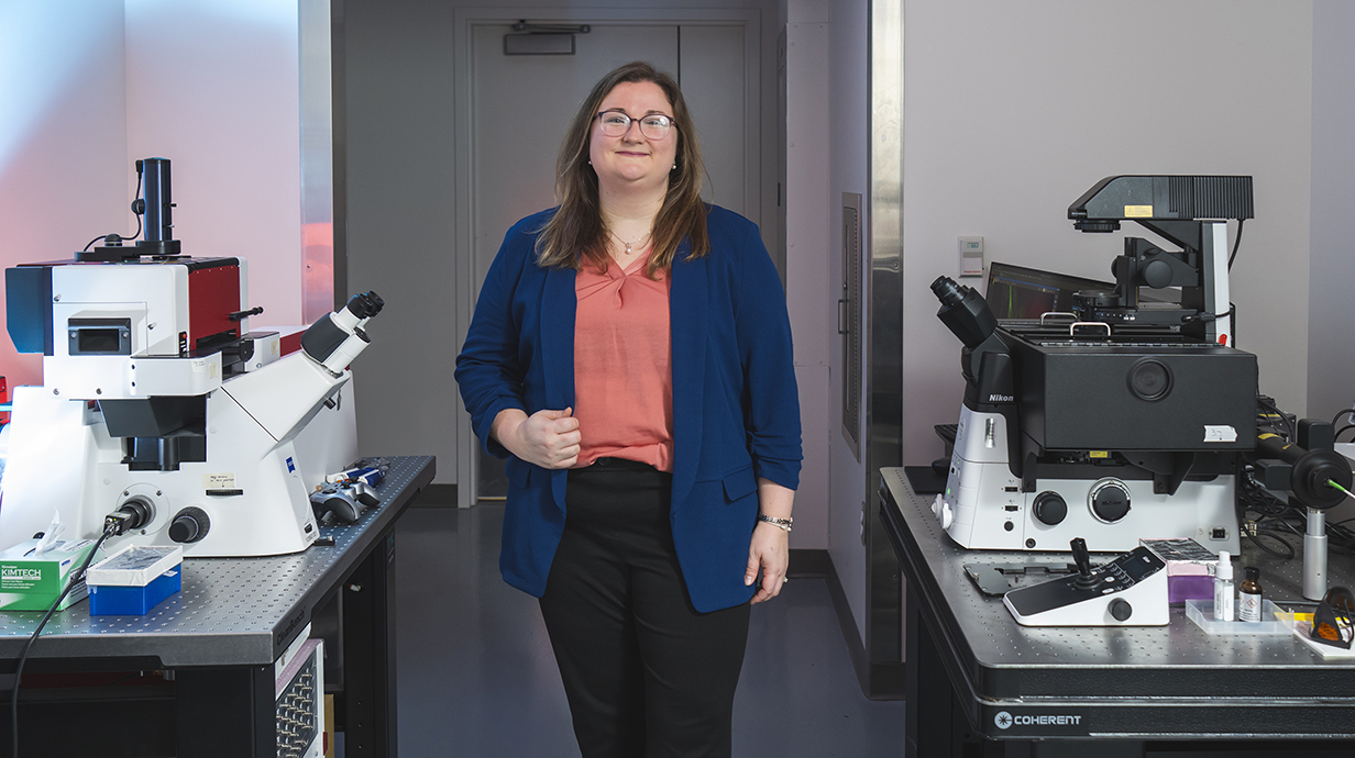 A woman wearing a blue jacket stands among tables filled with equipment in a lab.