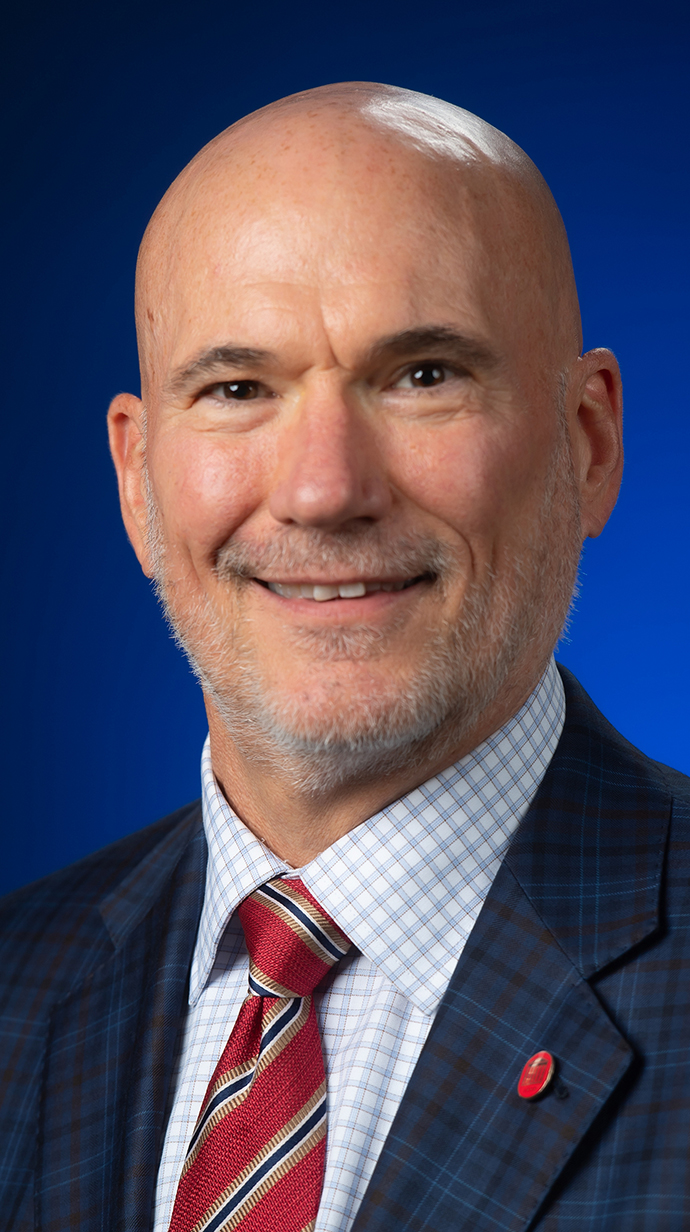Headshot of a man wearing a dark blue suit and a red tie.