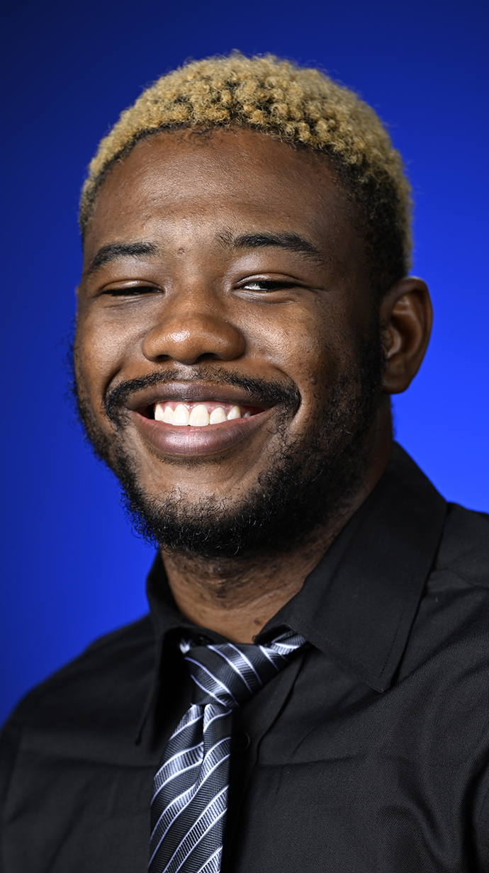 Headshot of a young man wearing a black shirt and a black-and-gray striped tie.