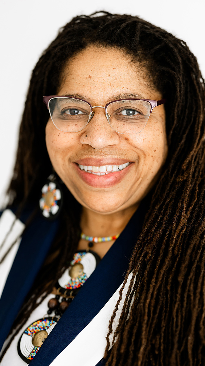Headshot of a woman with braided hair wearing colorful jewelry.