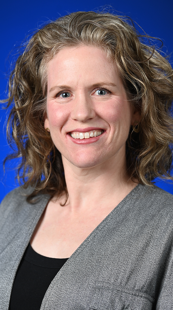 Headshot of a woman wearing a gray jacket over a black blouse.