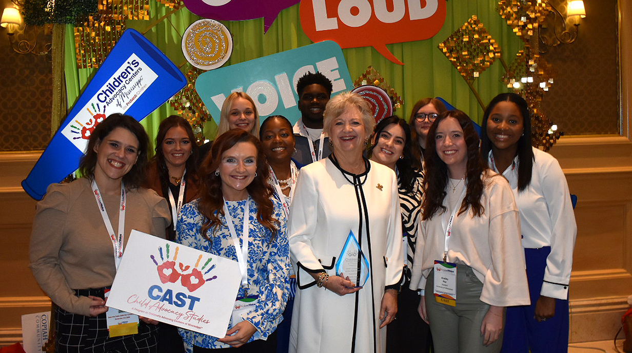 A group of young people surround a woman holding a crystal trophy in a conference hall.