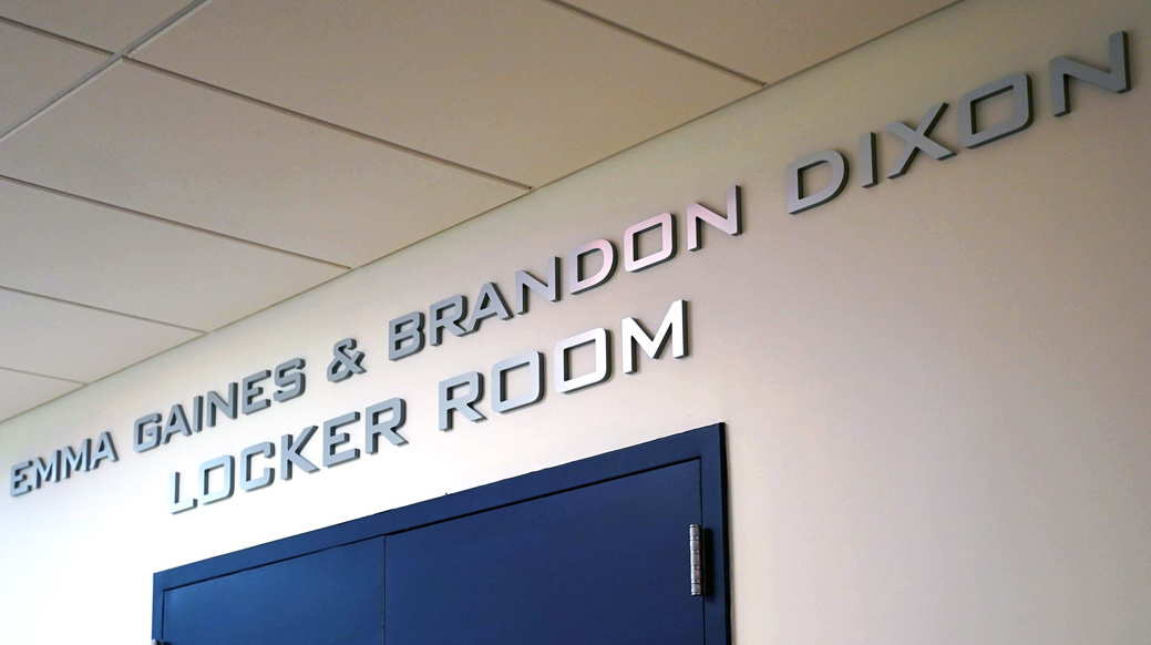 Signage above two blue doors reads 'Emma Gaines & Brandon Dixon Locker Room.'