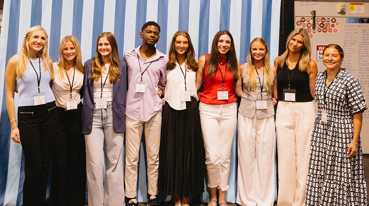 A group of young people stands in front of a blue-and-white striped backdrop.