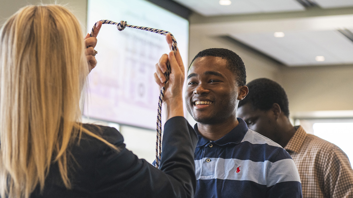 A woman presents a young man with a ceremonial cord.