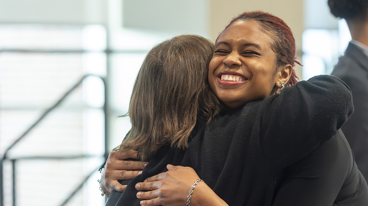 A woman smiles with her eyes closed as she embraces another woman.