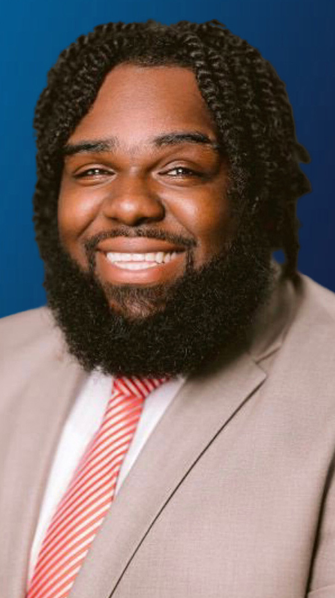 Headshot of a man wearing a tan suit and a red tie.
