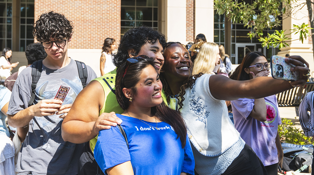 Three young women pose for a selfie together on an outdoor plaza.