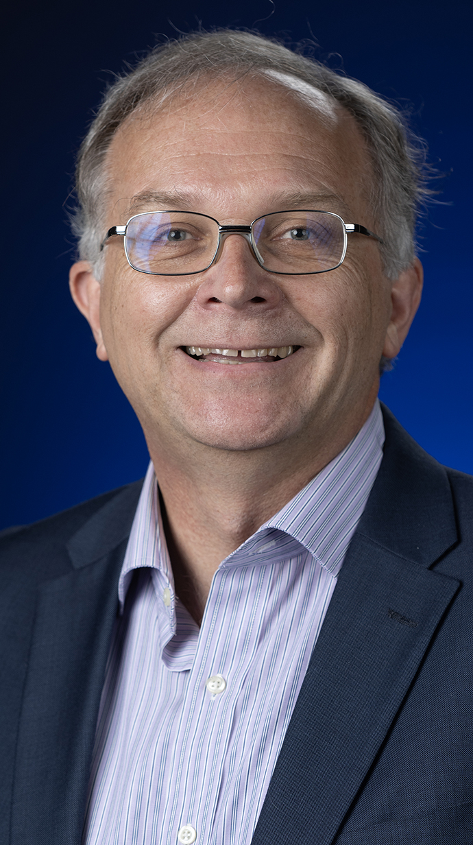 Headshot of a man wearing a dark blue jacket over a striped shirt.