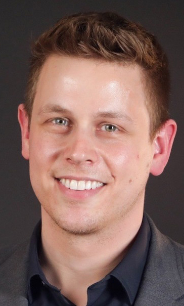 Headshot of a man wearing a gray jacket over a black shirt.