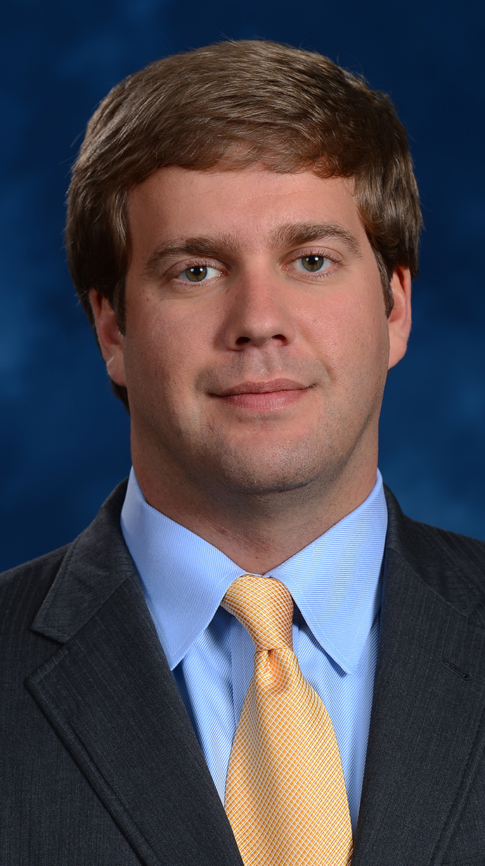 Headshot of a man wearing a dark suit with a yellow tie.