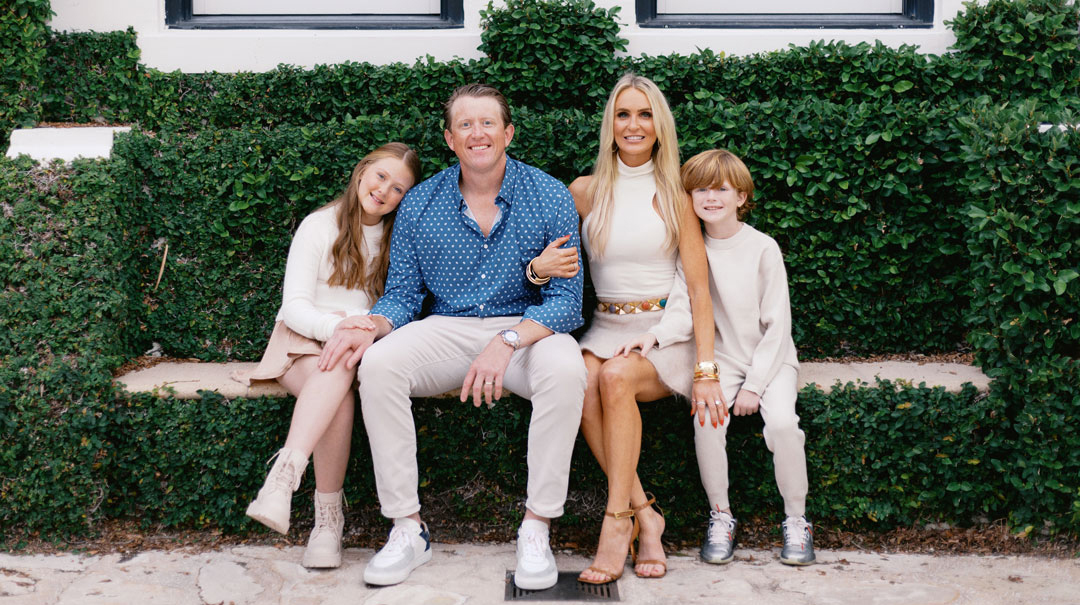 A man, woman, boy and girl pose for a family photo on an outdoor bench.