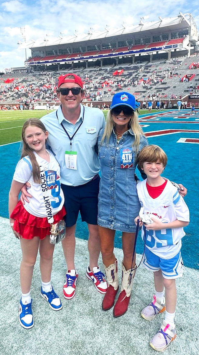 A family stands on the field in a nearly empty football stadium.