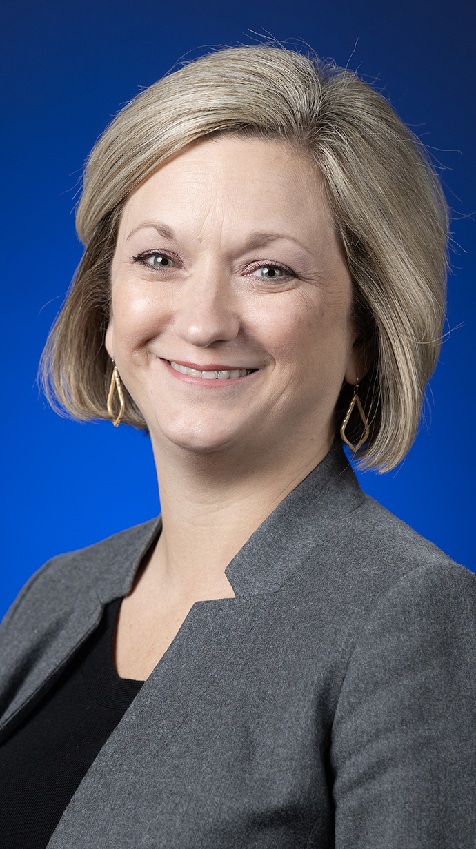 Headshot of a woman wearing a gray jacket over a black blouse.