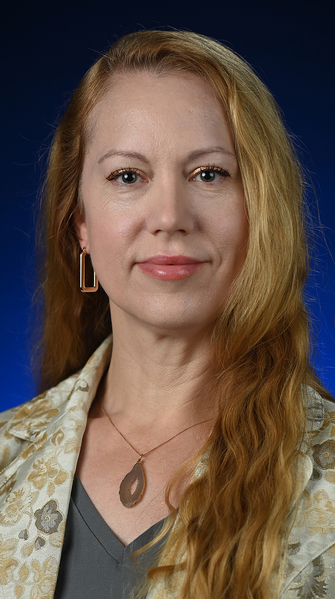 Headshot of a woman wearing floral patterned jacket over a gray blouse.