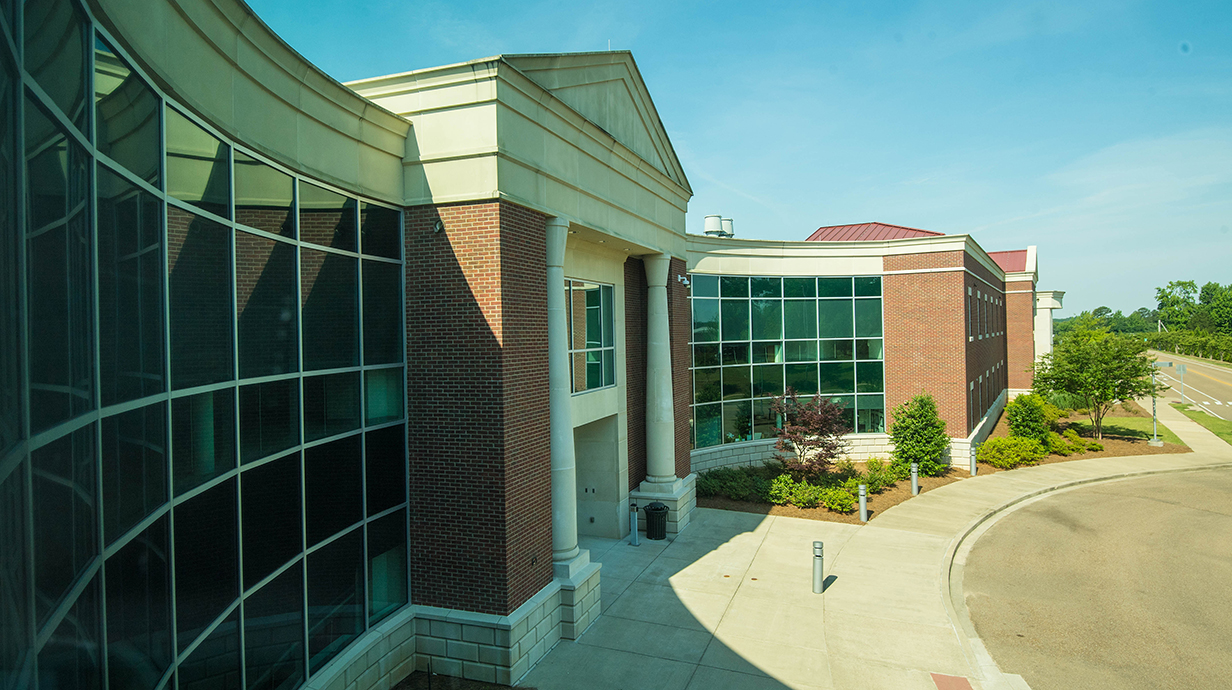 Photo of a two-story brick building with a curved facade lined with concrete panels and large glass windows.