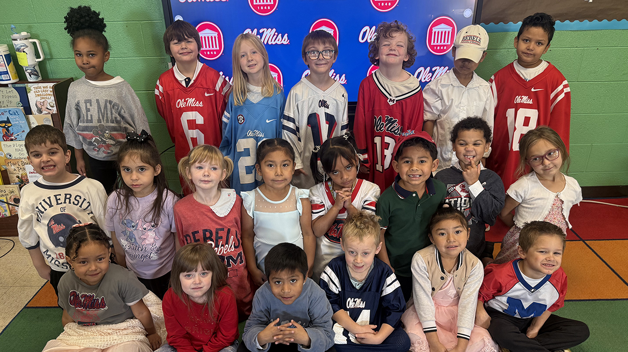 A group of children, all wearing Ole Miss apparel, sit in a school classroom.