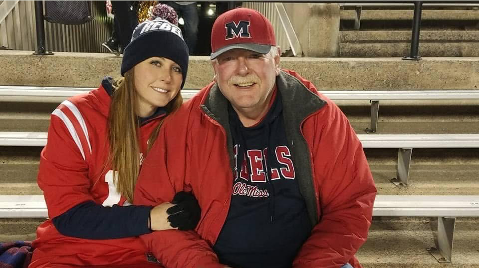 A man and a woman wearing cold-weather gear sit on bleachers in a stadium.