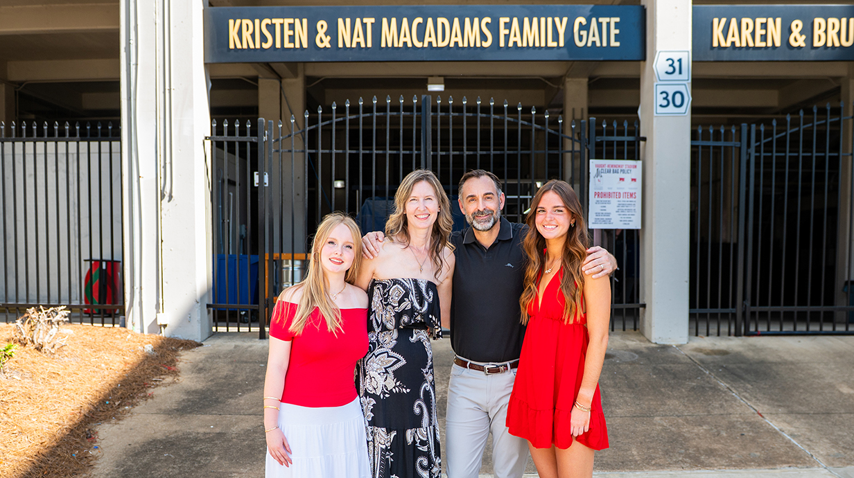 A man, a woman and two young women stand in front of an entrance gate at a stadium.