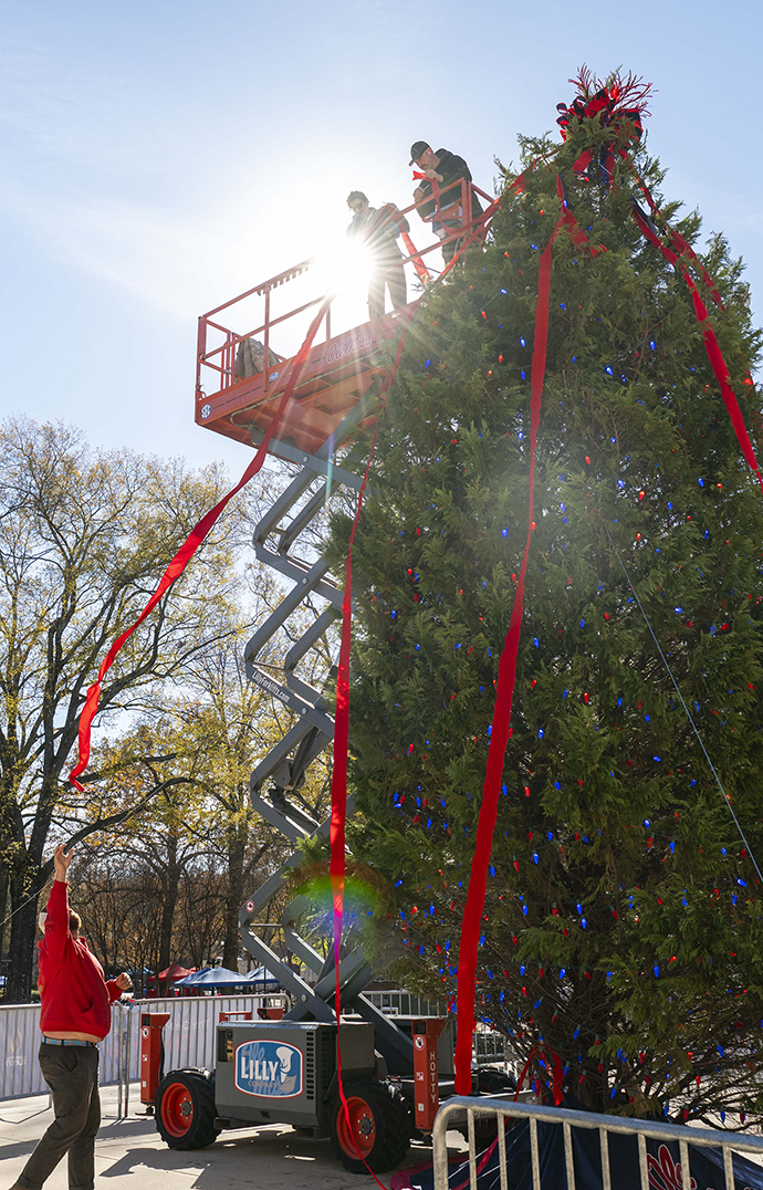 Workers use a lift to decorate a 30-foot Christmas tree on an outdoor plaza.