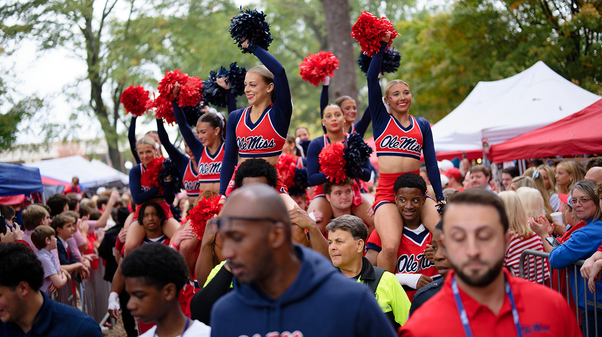 Cheerleaders and fans line a walkway in a park.