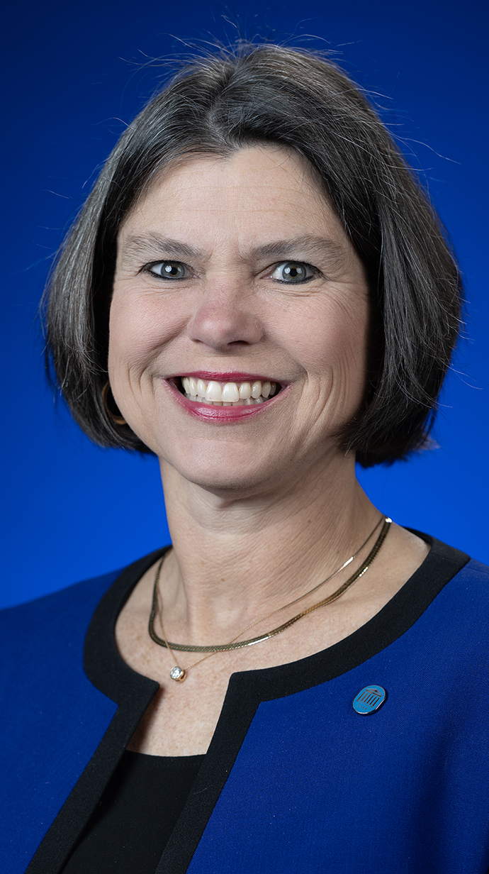 Headshot of a woman wearing a blue jacket over a black blouse.