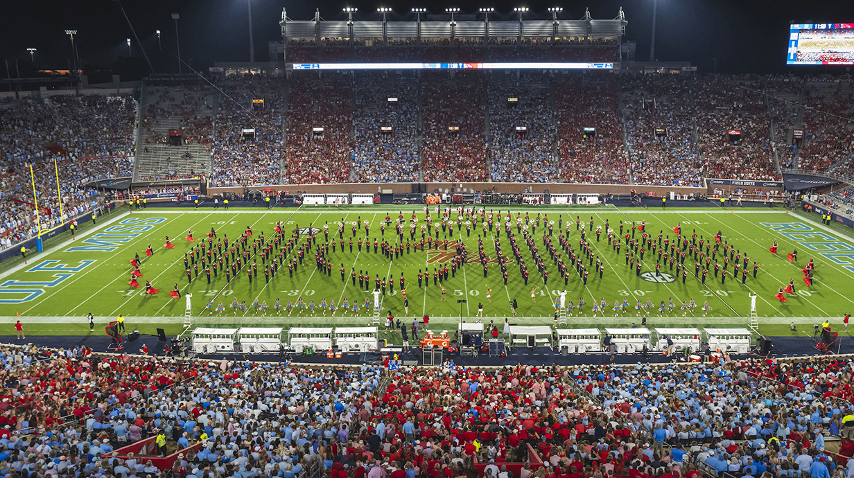 A college marching band performs a halftime show in a stadium.