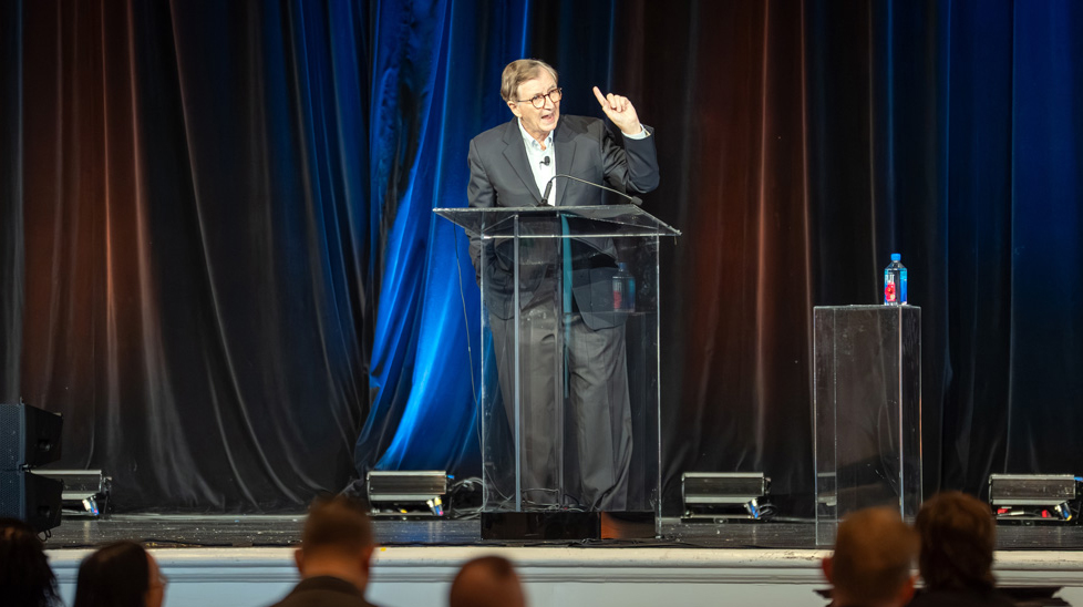 A man speaks from a podium in a conference hall.