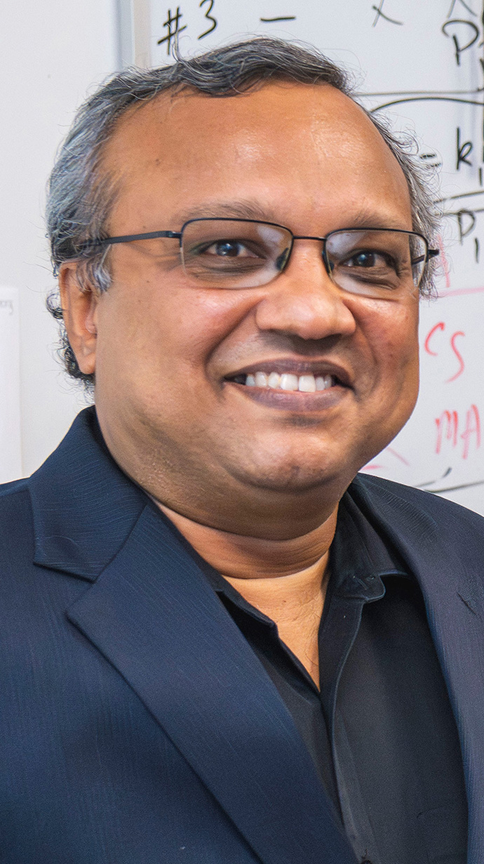Headshot of a man wearing a dark blue suit coat over a black shirt.