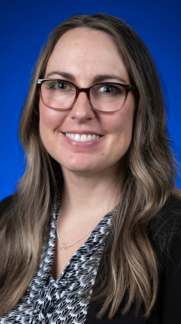 Headshot of a woman wearing a black jacket over a black-and-white patterned shirt.