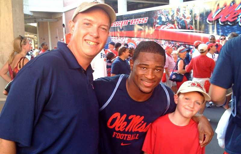 A man and a young boy take a photo with a football player.