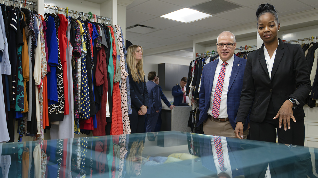 A man and a woman look at a display case near racks of clothing.